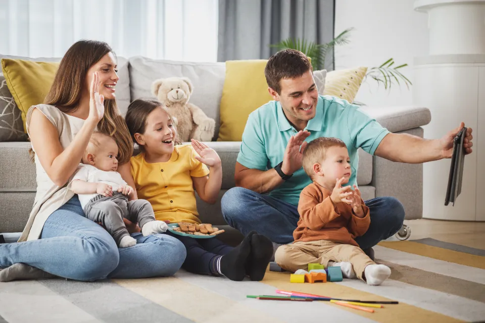 Eltern sitzen mit ihren drei kleinen Kindern auf dem Boden und spielen.