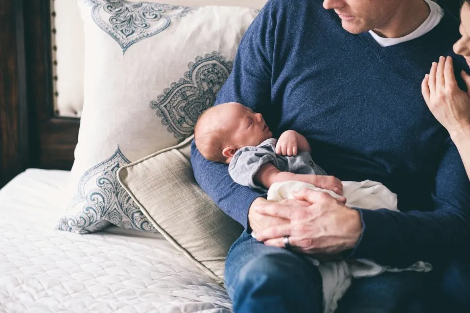 Ein Vater hält sein neugeborenes Kind im Arm, die Hand der Mutter liegt daneben.