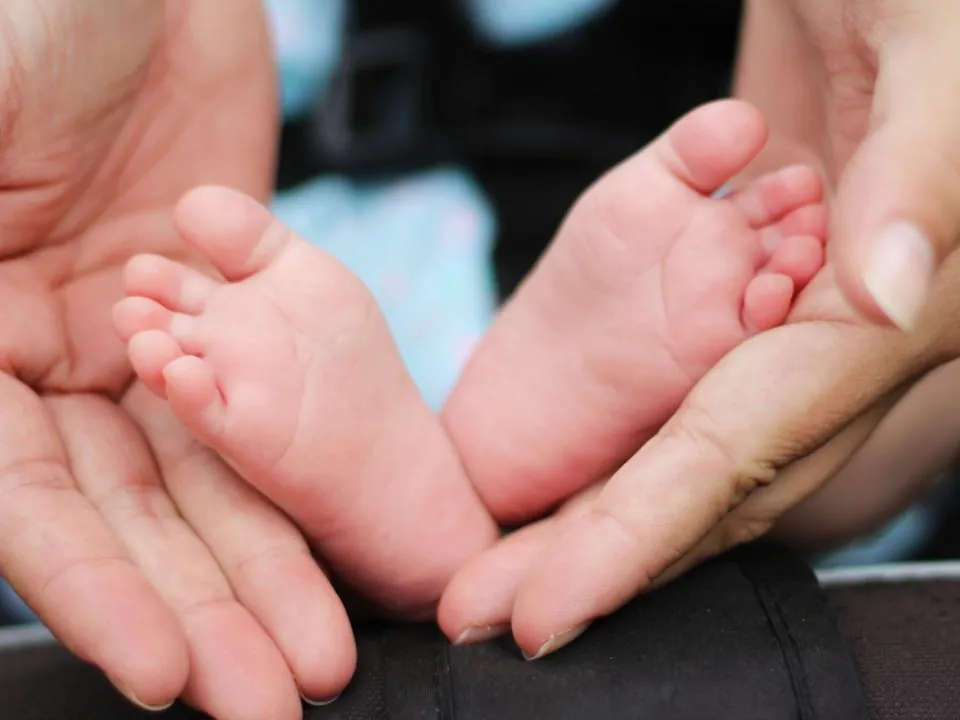 Die Füße eines Babys in den Händen eines Elternteils.